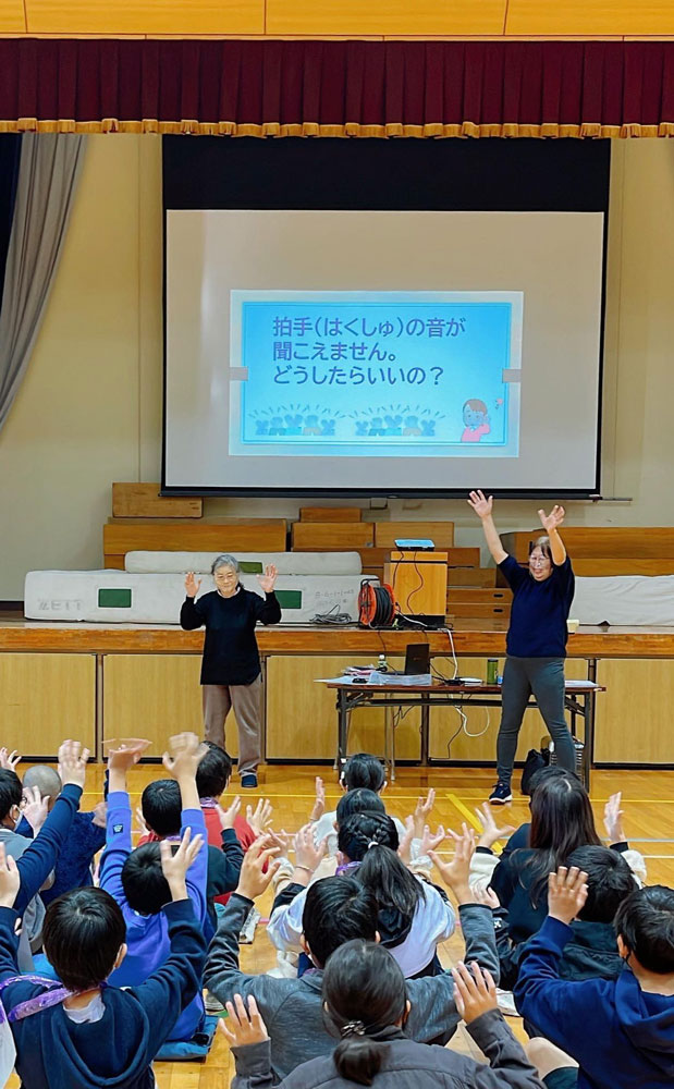 小学校への出前講座の様子。体育館で子どもたちが手を動かしながら講座を受けている様子。