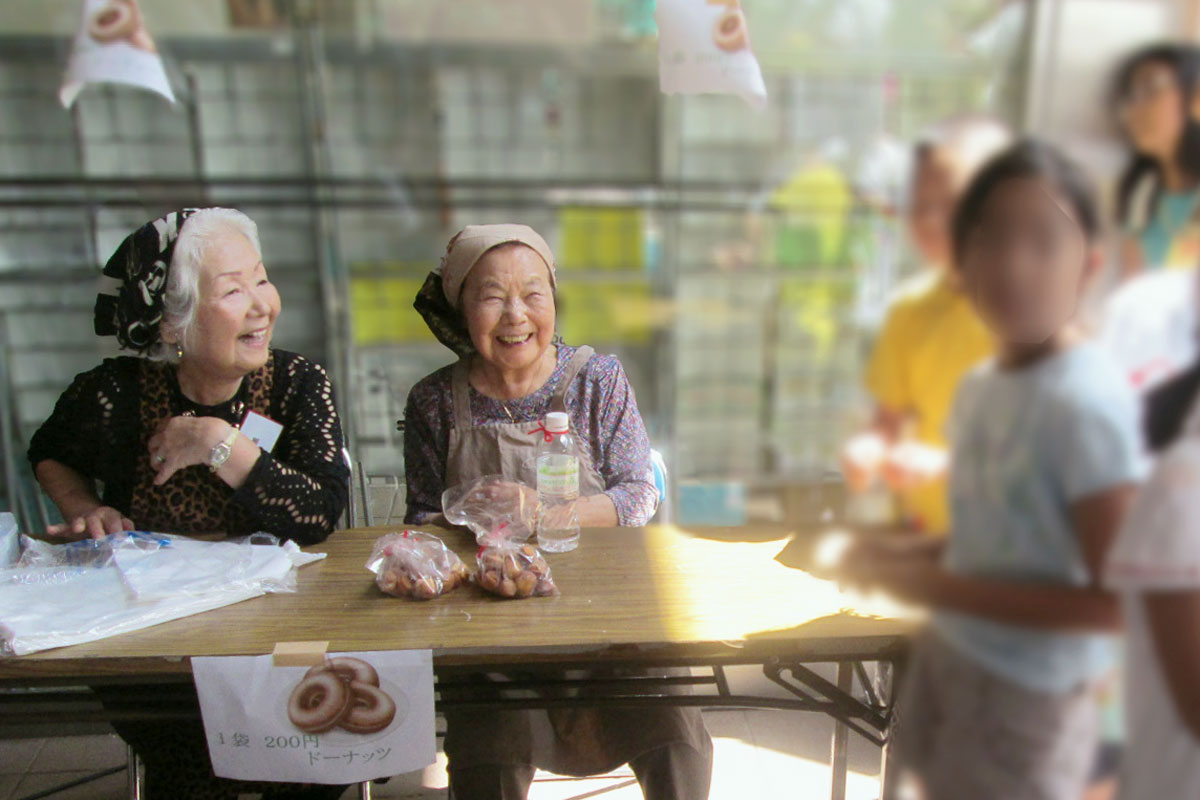 子どもたちにドーナツを販売する笑顔のおばあちゃんたちの写真
