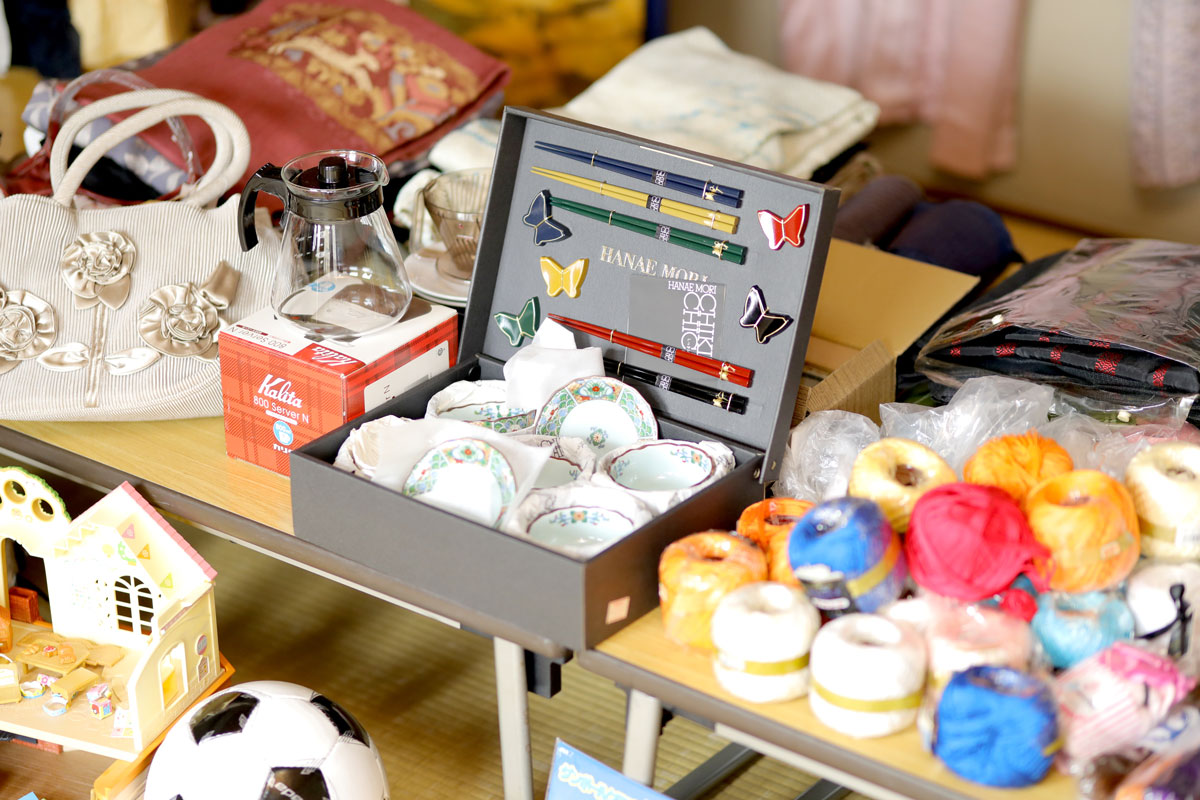 食器セットやコーヒーポッド、バッグ、サッカーボールなどのバザーの品が並んでいる。