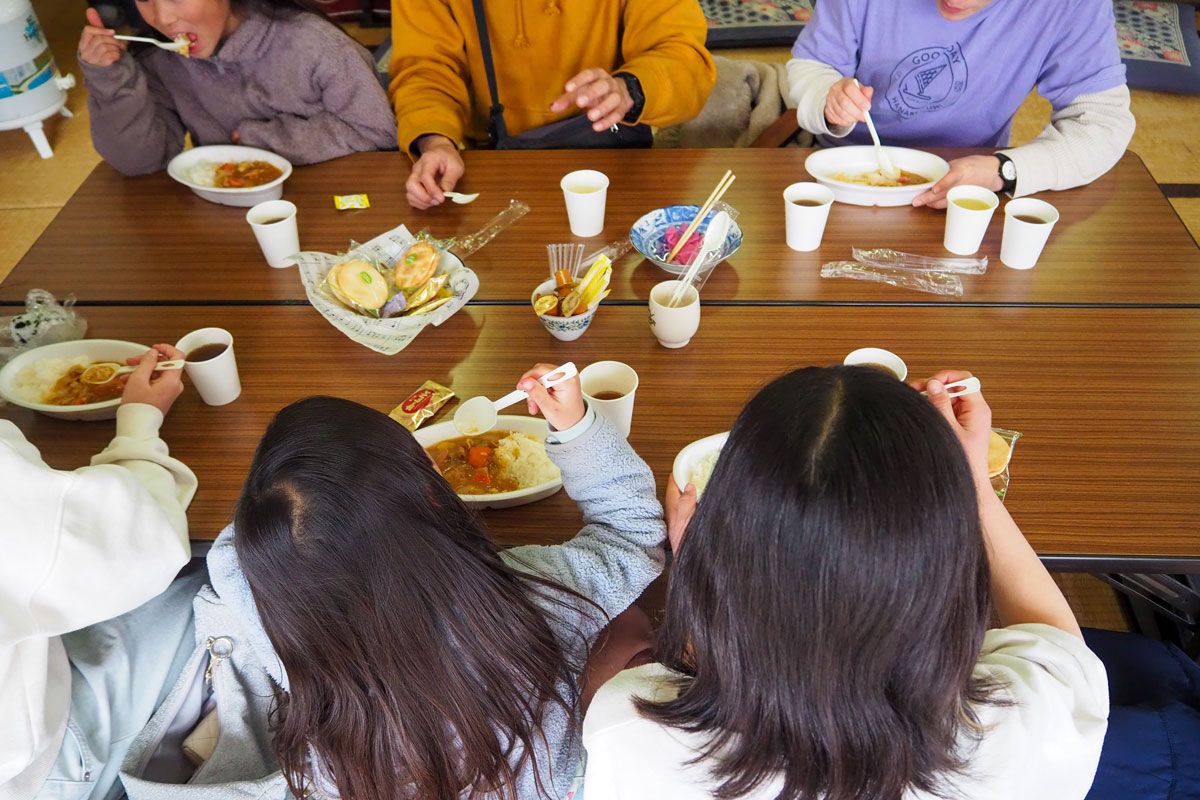 机を囲んで、カレーを頬張る子どもたちと大人。